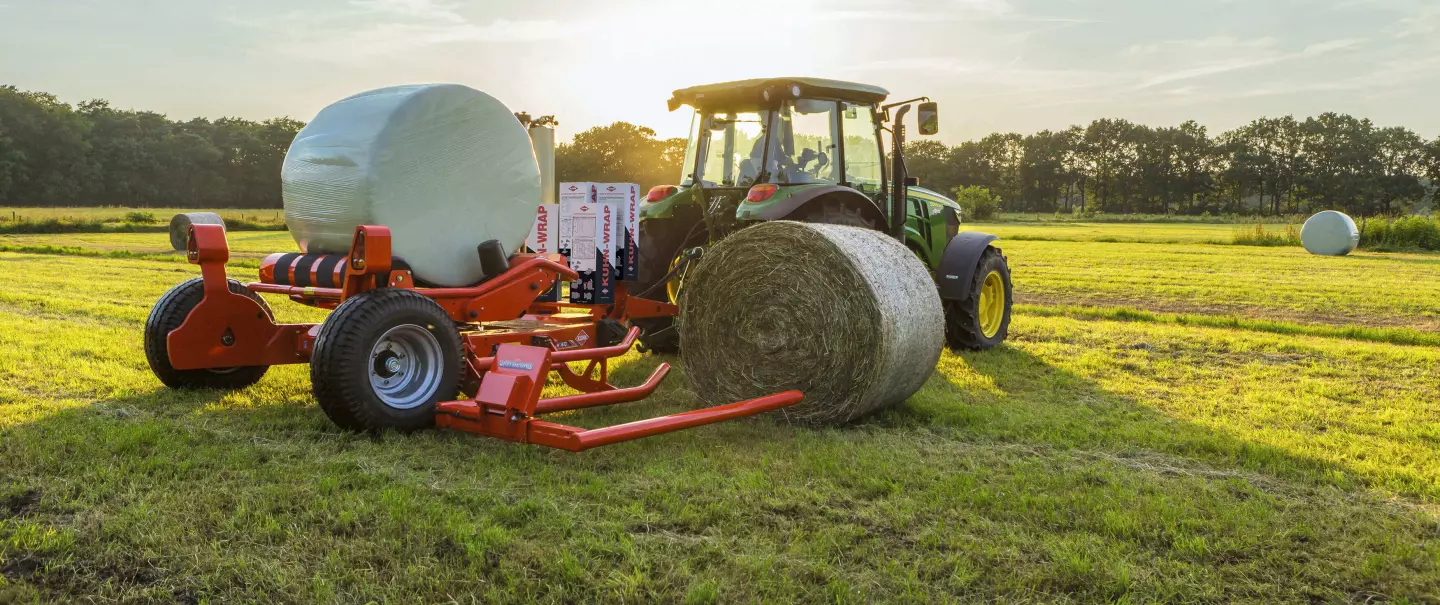 A empacotadora de fardos cilíndricos rebocada RW 1610 carregando um fardo cilíndrico durante a embalagem de outro fardo.